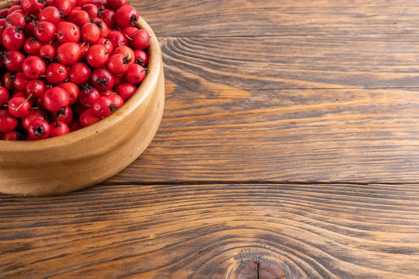 red hawthorn berries in wooden bowl on flat wooden surface.