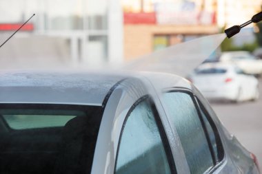 Yüksek basınçlı su temizleyicisiyle, kamu oto yıkama istasyonuna beyaz araba püskürterek, seçici bir odak ile yakın plan..