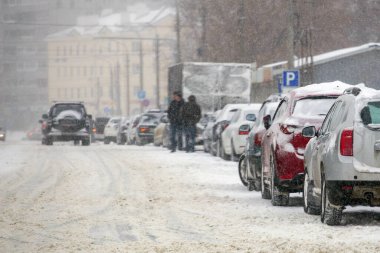 Gün ışığında yoğun kar fırtınası sırasında şehir yolunun kenarına park edilmiş bir arabanın yanına..