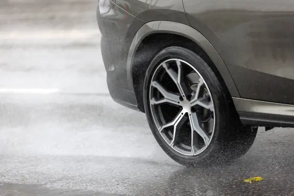 rain water splash flows from wheels of grey car that moving fast on asphalt road.