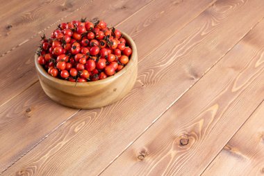 Tahta bir kasede, ahşap bir yüzey üzerinde kırmızı gül güllü meyveler.