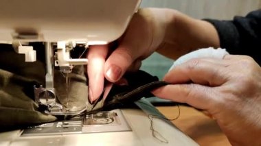 Bandajlı bir parmağı olan yaşlı bir kadın eli dikiş makinesiyle evde dikiliyor.