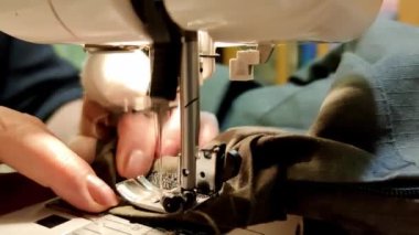 Bandajlı bir parmağı olan yaşlı bir kadın eli dikiş makinesiyle evde dikiliyor.