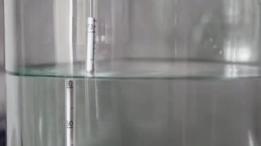 alkol damıtma işlemi yakın çekim - sıvı damıtılmış şeffaf sıvı içinde yüzen alkoholometre ile büyük cam kavanozda akıyor.