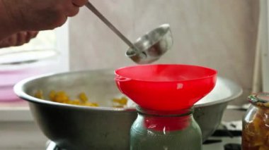 Kadın elleri cam kavanozları kırmızı huni ve çorba kepçesiyle elma reçeli ile dolduruyor. Yavaş çekimde seçici bir odaklanma ile kapanıyor.