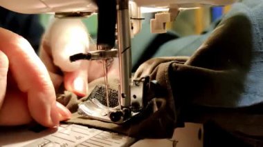 Bandajlı bir parmağı olan yaşlı bir kadın eli dikiş makinesiyle evde dikiliyor.