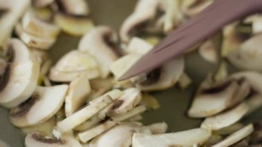 Taze şampiyon mantarları kızartılmış tavada plastik spatula ile karıştırılıyor, yavaş çekim yakın plan..