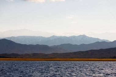 Sonbahar öğleden sonra Issyk-Kul Gölü 'ndeki mavi sakin su ve arka planda dağlar.