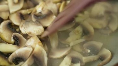 Taze şampiyon mantarları kızartılmış tavada plastik spatula ile karıştırılıyor, yavaş çekim yakın plan..