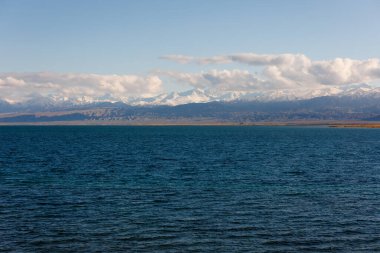 Sonbahar öğleden sonra Issyk-Kul Gölü 'ndeki mavi sakin su ve arka planda dağlar.