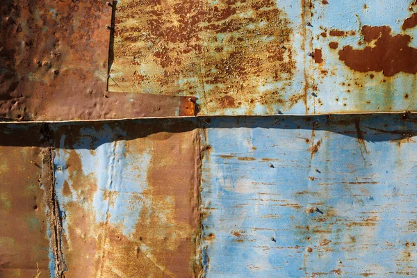 Paslı çelik çarşaflar ve kabuğu soyulmuş mavi boya kalıntıları. Arka planda yakın plan ve doğrudan güneş ışığı altında doku.