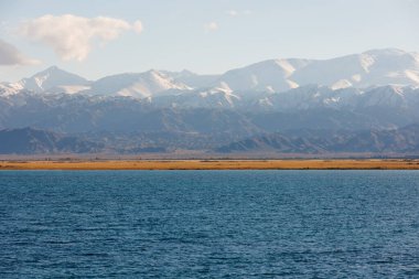 Sonbahar öğleden sonra Issyk-Kul Gölü 'ndeki mavi sakin su ve arka planda dağlar.