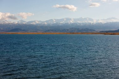 Sonbahar öğleden sonra Issyk-Kul Gölü 'ndeki mavi sakin su ve arka planda dağlar.