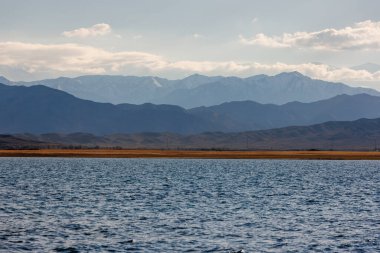 Sonbahar öğleden sonra Issyk-Kul Gölü 'ndeki mavi sakin su ve arka planda dağlar.