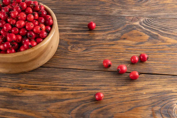 red hawthorn berries in wooden bowl on flat wooden surface.