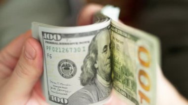 Beyaz eller, seçici odaklanma ve yavaş çekim ile yakın plan 100 Amerikan doları banknotlarını tutuyor ve kontrol ediyor.