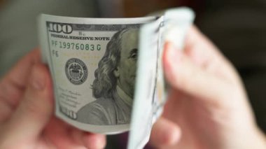 Beyaz eller, seçici odaklanma ve yavaş çekim ile yakın plan 100 Amerikan doları banknotlarını tutuyor ve kontrol ediyor.