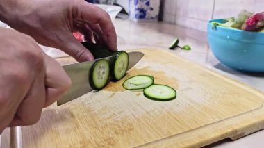 Beyaz eller, yerli mutfağın bambu kesme tahtasındaki kısa yeşil salatalıkları kesiyor. Geniş açılı, yavaş çekimde. Kullanıcı tarafından oluşturulan gerçek yaşam içeriği.