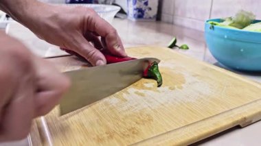 Beyaz eller, yerli mutfakta bambu kesme tahtasında uzun kırmızı tatlı biber kesiyor. Geniş açılı, yavaş çekimde. Kullanıcı tarafından oluşturulan gerçek yaşam içeriği.