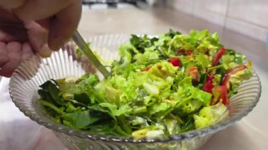 Beyaz eller sebze salatasıyla mayonezi cam bir kasede karıştırıyor ve ev mutfağında paslanmaz çelik çatal kullanıyor.