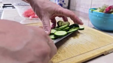 Beyaz eller, yerli mutfağın bambu kesme tahtasındaki kısa yeşil salatalıkları kesiyor. Geniş açılı, yavaş çekimde. Kullanıcı tarafından oluşturulan gerçek yaşam içeriği.