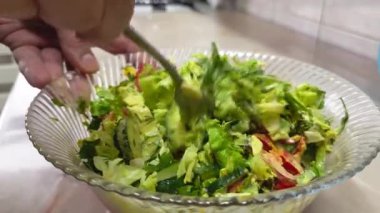 Beyaz eller sebze salatasıyla mayonezi cam bir kasede karıştırıyor ve ev mutfağında paslanmaz çelik çatal kullanıyor.