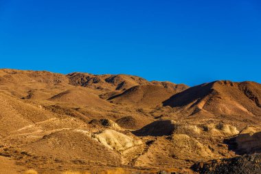 Kyrgyzstan landscape with a mountain range towering against a clear blue sky. The dried grasslands and gentle slopes create a natural horizon clipart