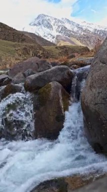 Bahar akşamında arka planda karla kaplı tepeleri olan dağ nehri..