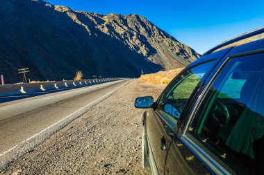 Asfalt yolda siyah motorlu araç, arka planda görkemli dağlar..