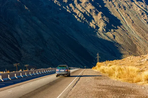 stock image Car is driving along the road through natural mountain landscape with concrete barrier at sunny autumn day in Boom Gorge, Kyrgyzstan - December 16, 2022