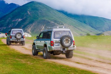 Engebeli dağ geçidi yolunda iki eski SUV, tozlu yolları terk ediyor, Semenovskoye vadisi, Kırgızistan 'da 5 Temmuz 2023' te macerayı ve keşfi sembolize ediyor.