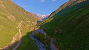 Baharda toprak yolu ve küçük deresi olan dağ geçidinin yeşil yamaçları, yavaş hava kulesi yüksekliği İHA görüntüsü..