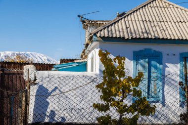 Kırgız kasabasında, açık mavi gökyüzünün altında, ufukta karla kaplı sıradağlarla kaplı, eğri büğrü çatılı taşralı bir ev..