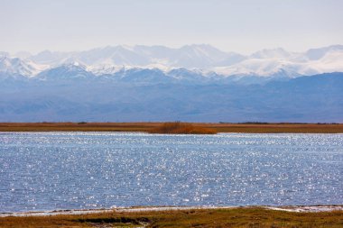 Sonbahar öğleden sonra Issyk-Kul Gölü 'ndeki mavi sakin su ve arka planda dağlar.