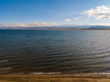 Sonbahar öğleden sonra Issyk-Kul Gölü 'ndeki mavi sakin su ve arka planda dağlar.