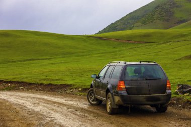Yağmurlu yaz gününde, dağlık tepelerde ıslak toprak yolun kenarında eski siyah bir araba.