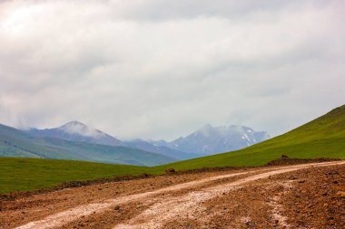 Kırgızistan 'da yağmurlu yaz gününde dağlarda toprak yol döner.