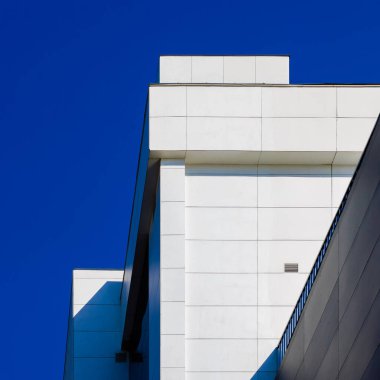 Bu, açık mavi gökyüzünün altındaki modern bir binanın geometrik yapısını gösteren sanatsal bir tasvirdir.