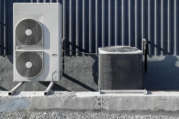 stock image Two different types of outdoor air conditioning units are installed outside a building, showcasing the benefits of modern cooling technology at sunny day