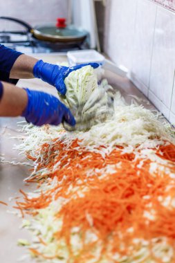 hands in blue gloves cutting cabbage with special double blade slit cabbage shredder knife during sauerkraut preparation clipart