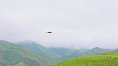 Çiseleyen yaz gününde sisli yeşil dağların üzerinde uçan ve dönen kuadkopter drone..