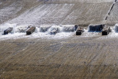 Bir sıra paraşüt, beton su sızıntısı kanalındaki blokları dengeleyerek suyun akışını yavaşlatır..