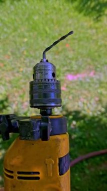 Ucuz, eğri büğrü bir Chinesium matkabı, güneşli bir günde yeşil çimlerin üzerine kurulmuş eski bir el yapımı elektrikli matkabın içinde dönüyor ve bütçe araçları kavramını vurguluyor..