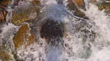 Kaynayan dağ nehri suyu kahverengi kayaları yıkıyor, yavaş çekim yakın çekim görüntüsü