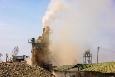 Gündüz vakti küçük asfalt fabrikalarından yükselen beyaz buhar ön planda çakıl yığınları ile.