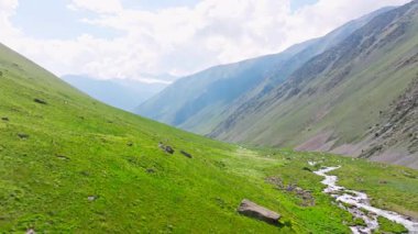 Kırgızistan 'da güneşli yaz gününde yeşil yamaçlı pitoresk dağ geçidi. Tian-Shan dağ sırasının üzerinde beyaz bulutlu mavi gökyüzü, Dolly ileri kamera hareketli drone bakış açısı.