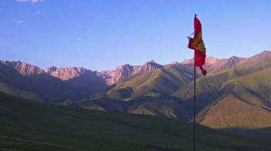 Kırgızistan 'daki görkemli dağların nefes kesici manzarası, rüzgarda hafifçe dalgalanan bayrağıyla.