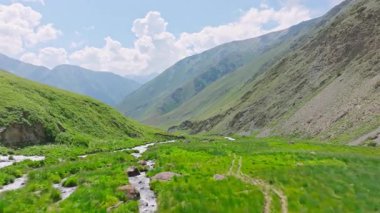 Kırgızistan 'da güneşli yaz gününde yeşil yamaçlı pitoresk dağ geçidi. Tian-Shan dağ sırasının üzerinde beyaz bulutlu mavi gökyüzü, Dolly ileri kamera hareketli drone bakış açısı.