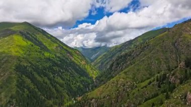 Mavi gökyüzünde beyaz bulutlu yeşil dağ yamaçları, drone hiperlapse