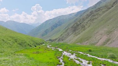 Kırgızistan 'da güneşli yaz gününde yeşil yamaçlı pitoresk dağ geçidi. Tian-Shan dağ sırasının üzerinde beyaz bulutlu mavi gökyüzü, Dolly ileri kamera hareketli drone bakış açısı.